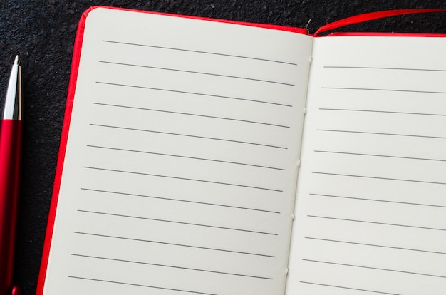 Empty red notebook with red pen on dark background