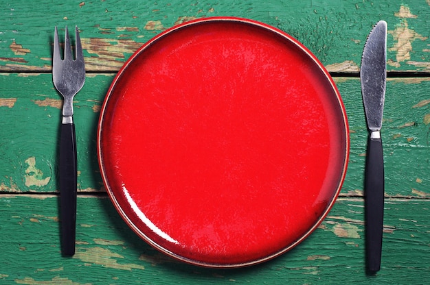 Empty red plate, fork and knife on old green table. Top view