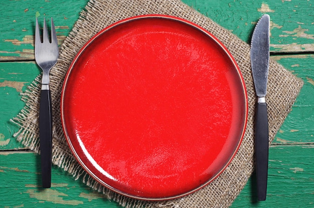 Empty red plate, fork and knife on old green table. Top view