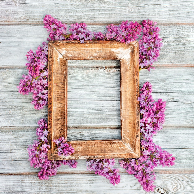 Empty retro wooden frame with spring branches of lilac flowers on a table of worn wooden white boards in a rustic style. Free space