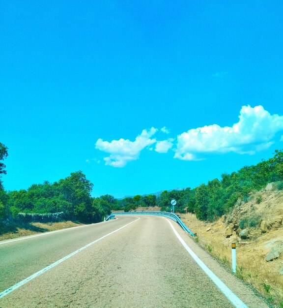 Empty road along trees and against blue sky