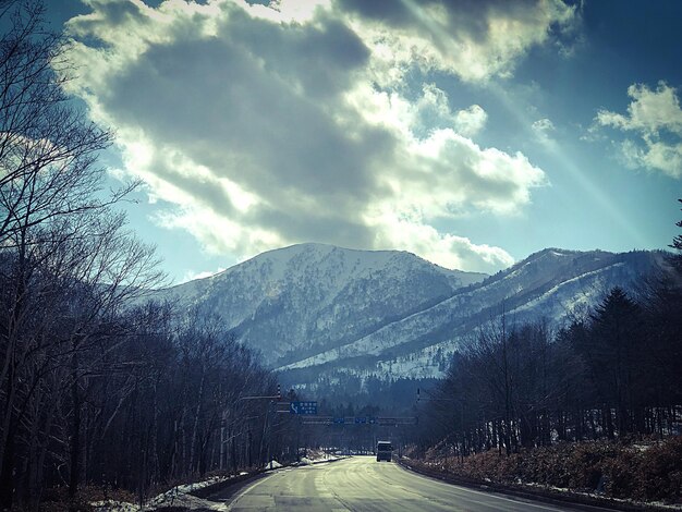 Empty road along trees and mountains against sky