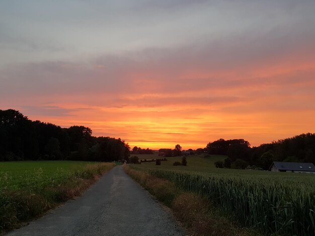 Empty road amidst field against sky during sunset