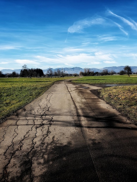 Empty road amidst field against sky