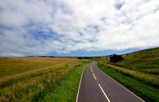 Empty road amidst field against sky