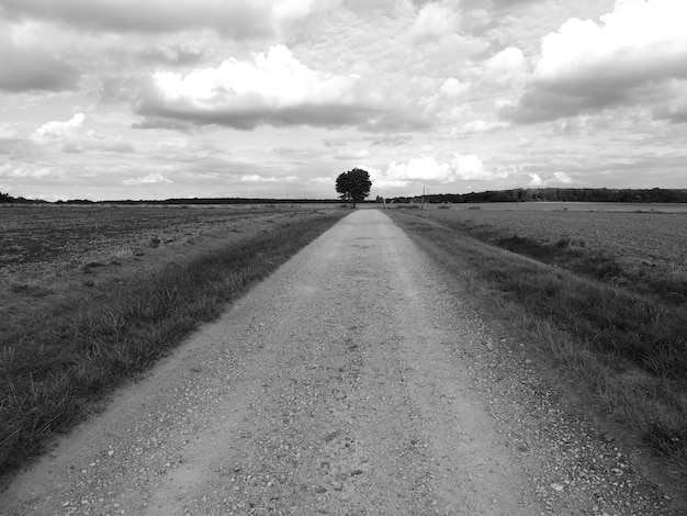 Empty road amidst field against sky