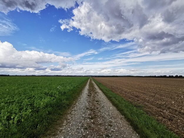 Empty road amidst field against sky