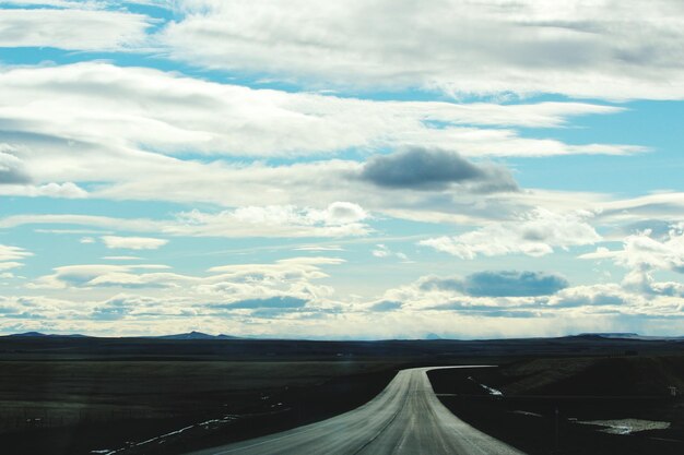 Empty road amidst landscape against cloudy sky