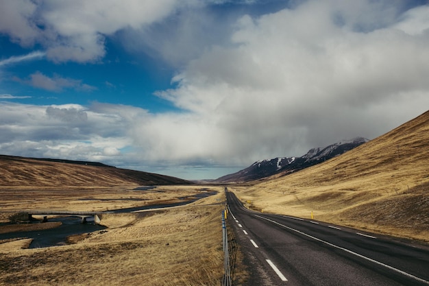 Empty road amidst landscape against cloudy sky