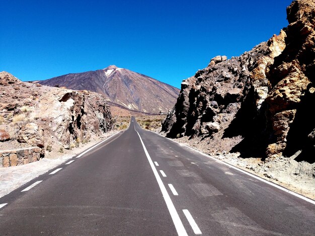 Empty road amidst mountains against clear blue sky