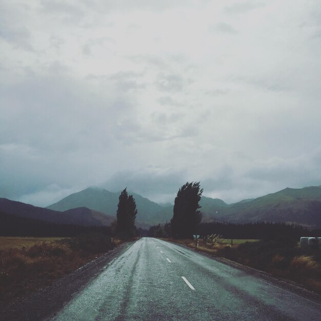 Empty road by mountains against cloudy sky