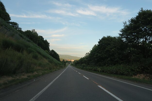 Empty road by trees against sky