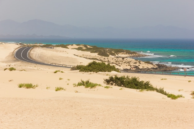 Foto strada vuota che attraversa il deserto delle dune di sabbia nel parco naturale di corralejo in riva al mare a fuerteventura