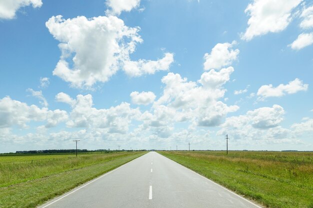 Empty road on grassy field against cloudy sky