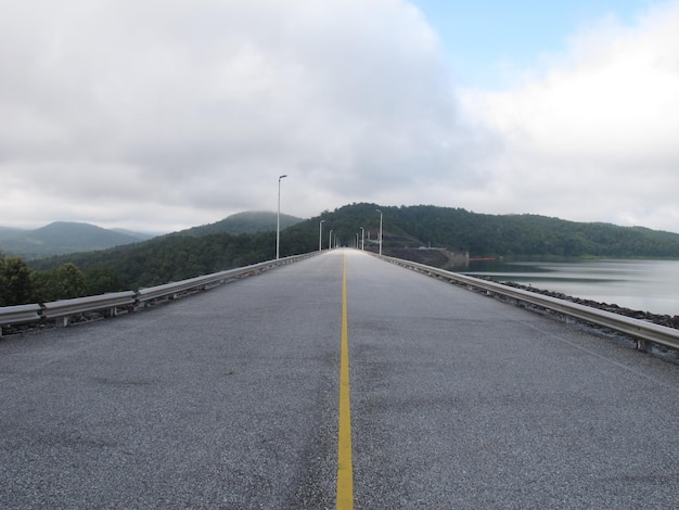 Empty road leading towards mountains against cloudy sky