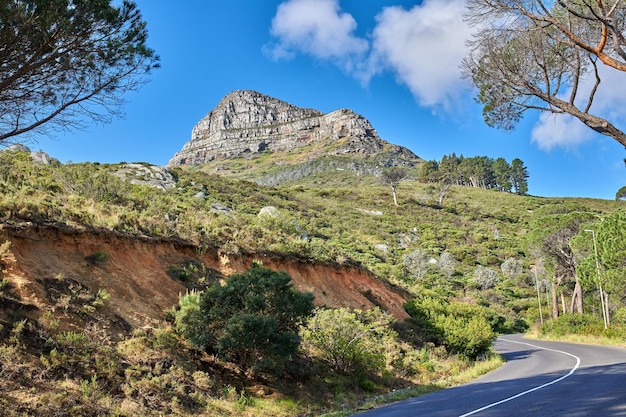 Empty road in the mountains with a cloudy blue sky Landscape of a countryside roadway for traveling on a mountain pass along a beautiful scenic nature drive with green trees and shrubs in Cape town