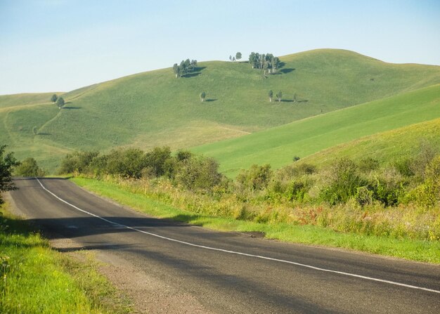 風景と空の道。アスファルト高速道路。緑の丘のある田園地帯の自然。旅行と旅。夏のルート。背景付きの高速道路ビュー。地平線の視点。田舎の旅と風景。