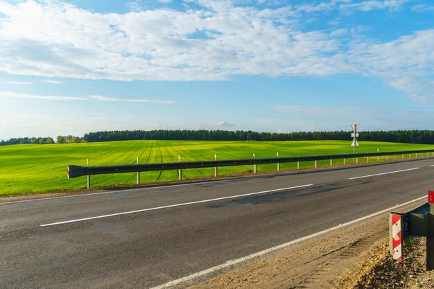 An empty roadway outside the city passes by a rural field and a\
blooming meadow travel by car away from the city and the hustle and\
bustle paved road on a sunny day without cars