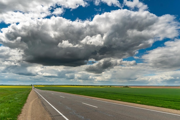 An empty roadway outside the city passes by a rural field and a blooming meadow Travel by car away from the city and the hustle and bustle Paved road on a sunny day without cars