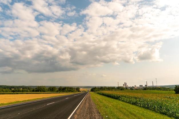 An empty roadway outside the city passes by a rural field and a\
blooming meadow travel by car away from the city and the hustle and\
bustle paved road on a sunny day without cars