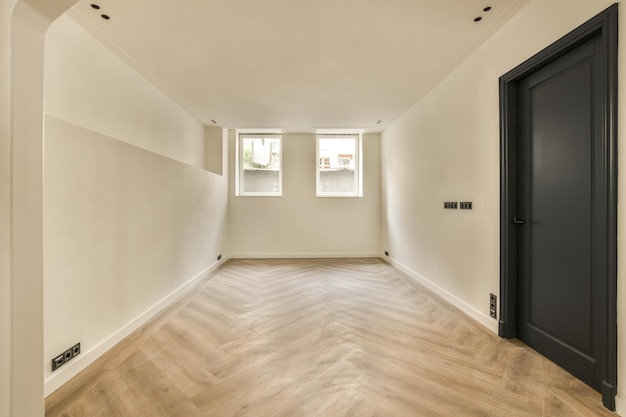 A empty room with a black door and two windows