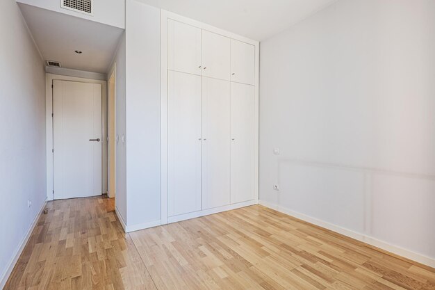 Empty room with a builtin wardrobe with white wooden doors with matching trunks and air conditioning ducts in the false ceiling