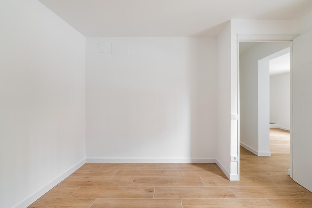 Empty room with laminate flooring and newly painted white wall with corridor leading to other rooms