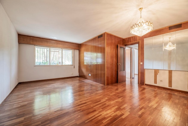 Foto stanza vuota con una parete ricoperta da un murale di vernice per legno in un colore che si abbina ai pavimenti in parquet, un'altra con specchi e un lampadario di cristallo sul soffitto