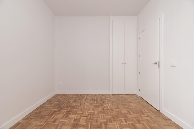 Пустая комната с небольшим новым встроенным шкафом с белыми деревянными раздвижными дверями
