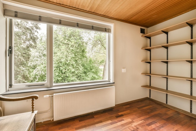 Foto una stanza vuota con pavimento in legno e scaffali sul muro c'è una finestra che si affaccia sugli alberi all'esterno