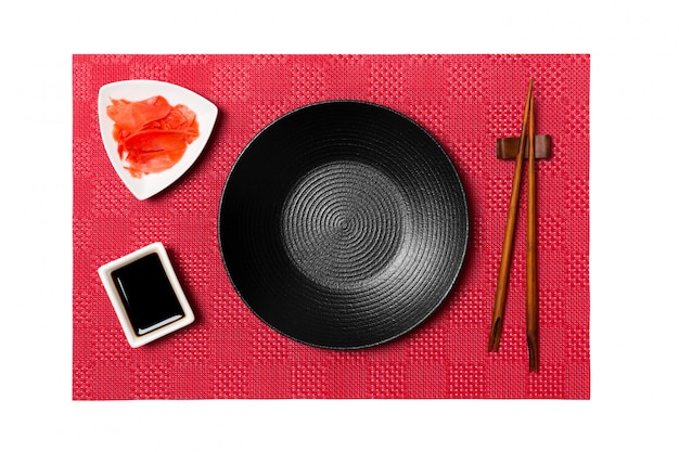 Photo empty round black plate with chopsticks for sushi and soy sauce, ginger on red mat sushi