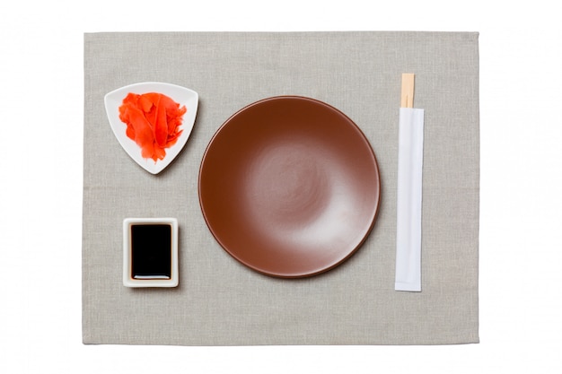 Empty round brown plate with chopsticks for sushi, ginger and soy sauce on grey napkin