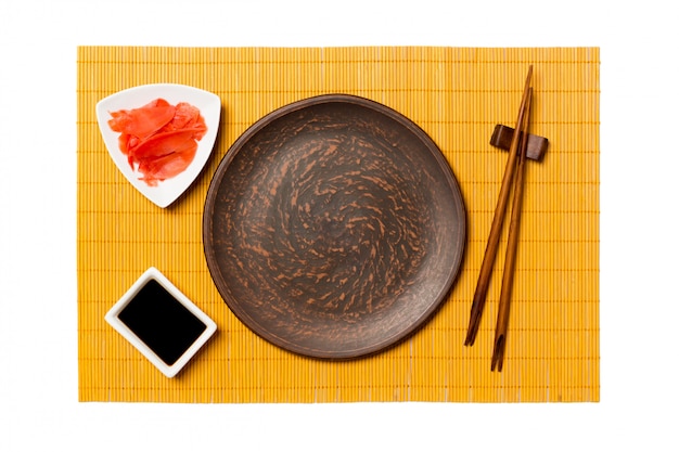 Empty round brown plate with chopsticks for sushi, ginger and soy sauce on yellow bamboo mat