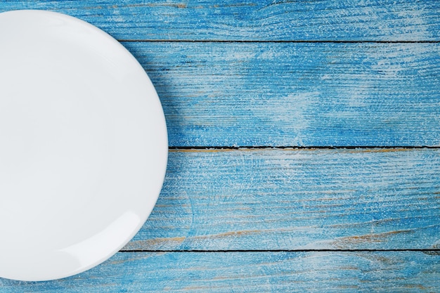 An empty round white plate on a blue wooden table. Top view