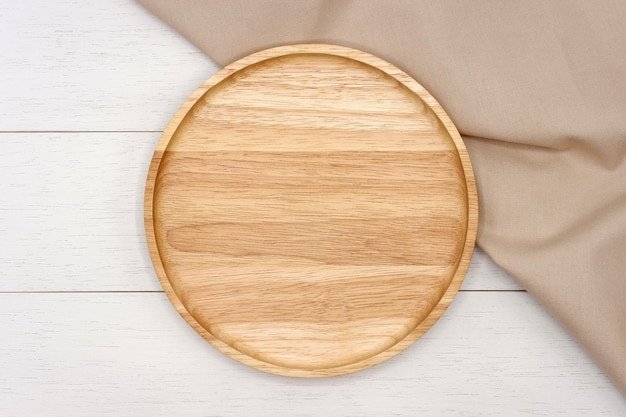 Empty round wooden plate with beige tablecloth on white wooden table Top view image