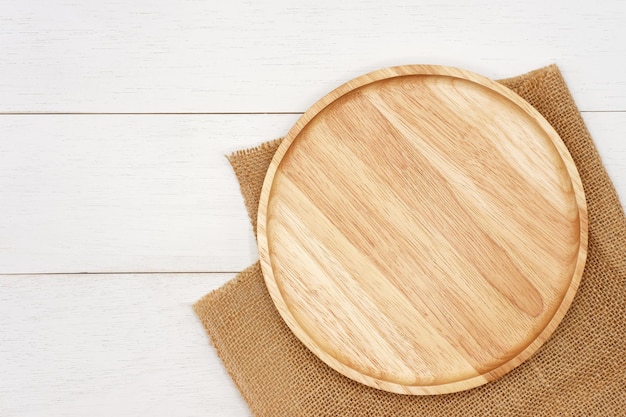 Empty round wooden plate with rustic brown burlap cloth on white wooden table Top view image