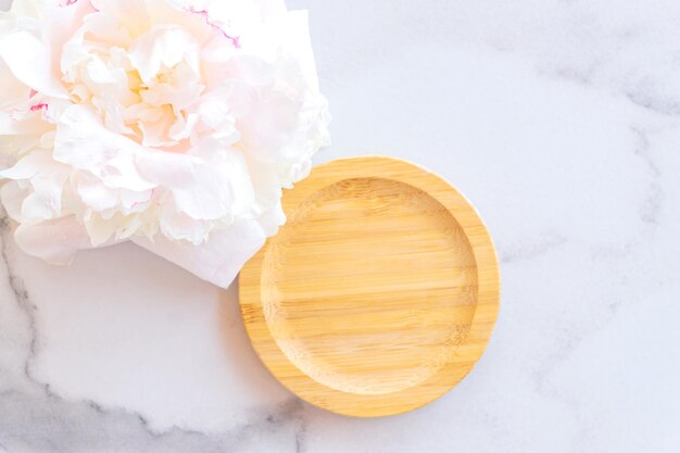 Empty round wooden podium for product presentation white peony on marble background Background of natural materials for cosmetic advertising closeup top view