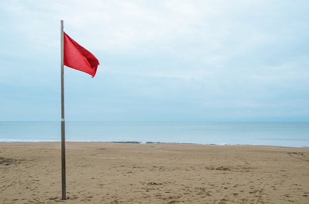 Empty sandy beach and red storm flag on a cloudy day.