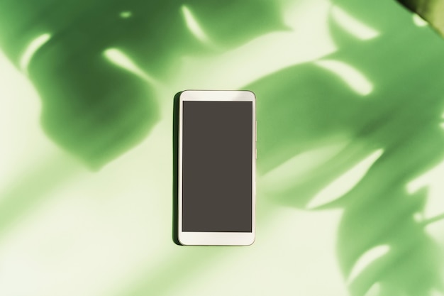 Photo empty screen smart phone with shadow of tropical green leave