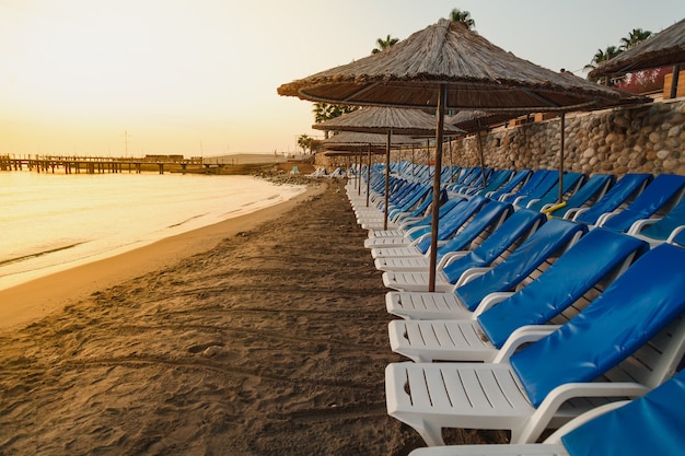 Empty sea beach with a flat row of sun beds and umbrellas at sunrise