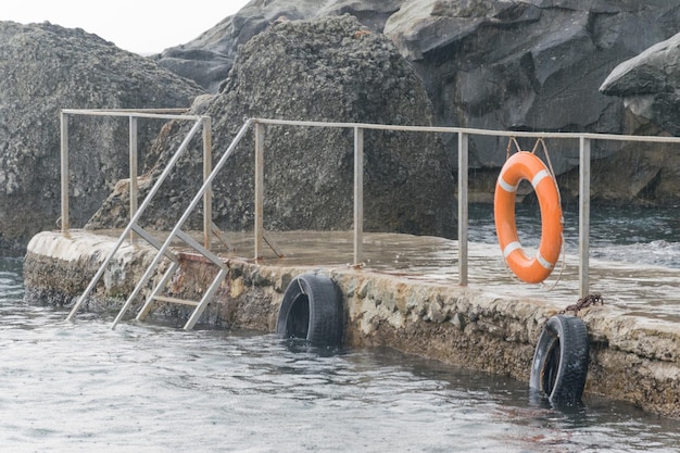 Empty sea pier surrounded by rocks during the rain with lifebuoys