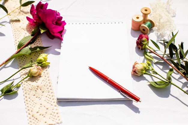 Empty sheet of paper in notepad with red pen laying on it Several flowers with buds placed near Creative mood concept