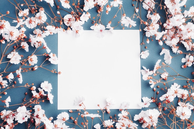 Empty sheet of paper surrounded by small white flowers. Blank card on blue background