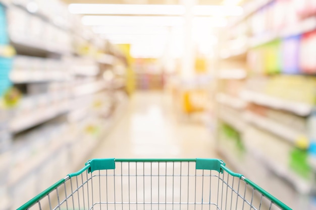 Empty shopping cart with blur supermarket store aisle and product shelves interior background