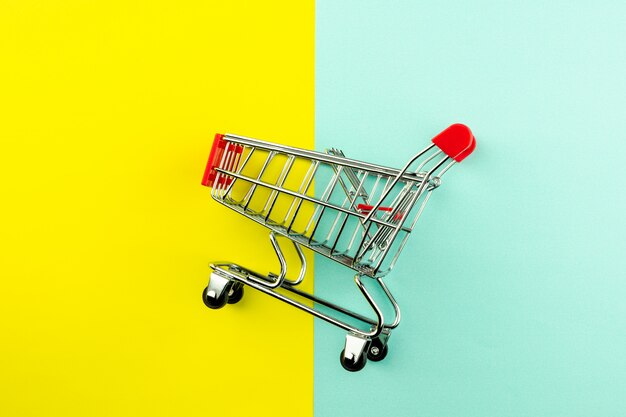 Photo empty shopping cart on yellow and blue background