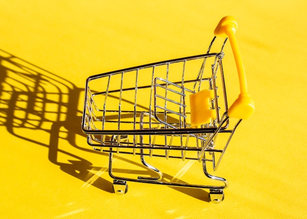 Empty shopping trolley on a bright refreshing yellow background. Colors of the year. Shopping concept.