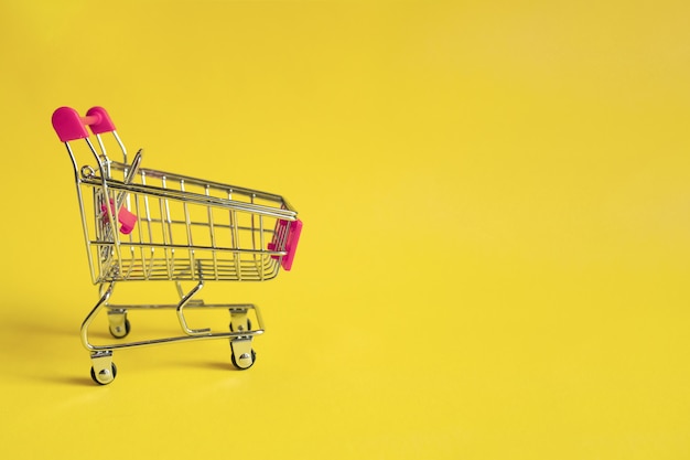 Empty shopping trolley with pink handle on yellow . Online shopping . A form of electronic commerce.