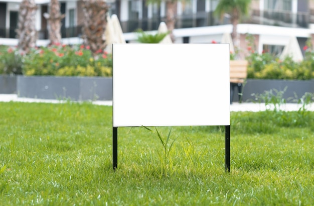 Empty sign advertising mockup banner on grass near pavement in city green parkCopy space for textInformation board on white background