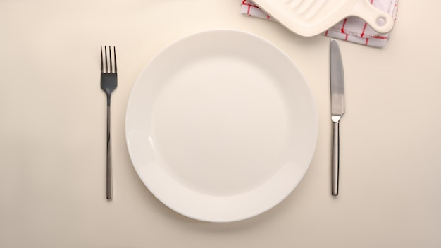 Empty simple white ceramic plate with silverware on white table, top view, flat lay