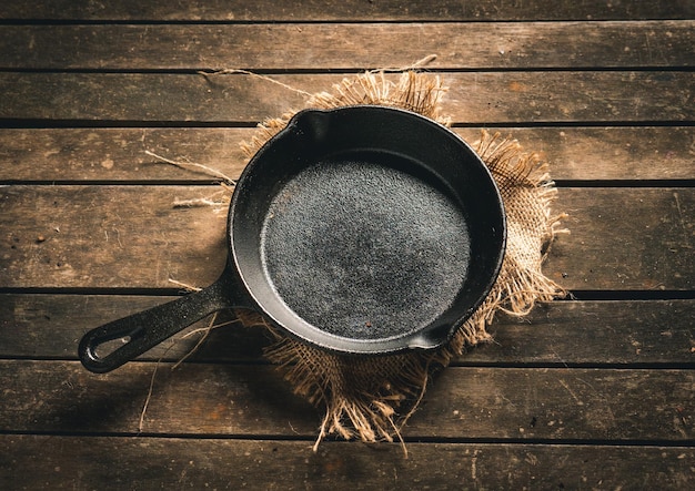 Empty small iron skillet on sackcloth on aged brown wooden table